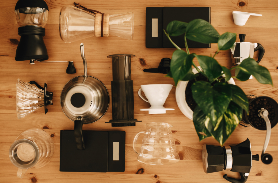 Picture of various coffee brewers including, espresso maker, coffee, pour-over set, scale, kettle, and areopress on a wooden counter