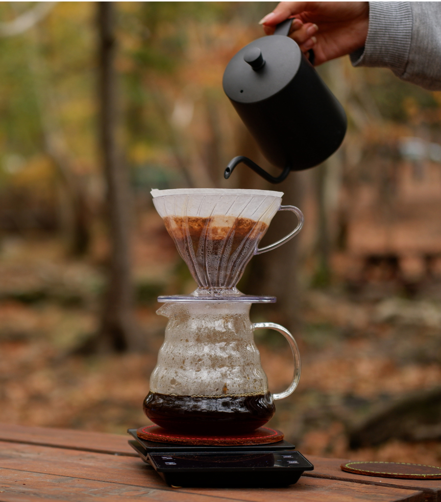 Picture of a person using a pour-over coffee set in an outdoor campsite setting, 